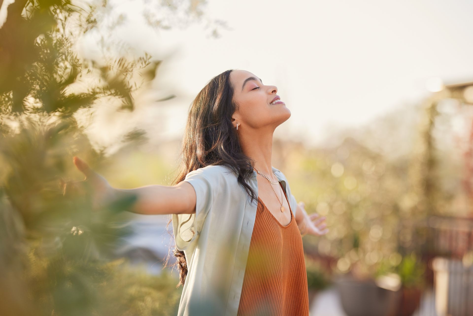 A woman outdoors with arms open and eyes closed, enjoying the sun